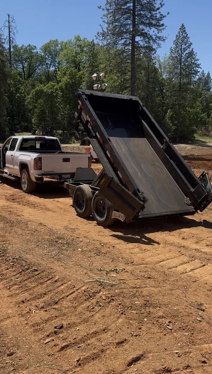 Stress Less Removal truck with its dump trailer raised on a dirt jobsite